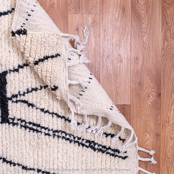 White Moroccan wool rug with abstract black diamond design, handwoven by Berber artisans, displayed on a wooden floor. Perfect for modern decor.