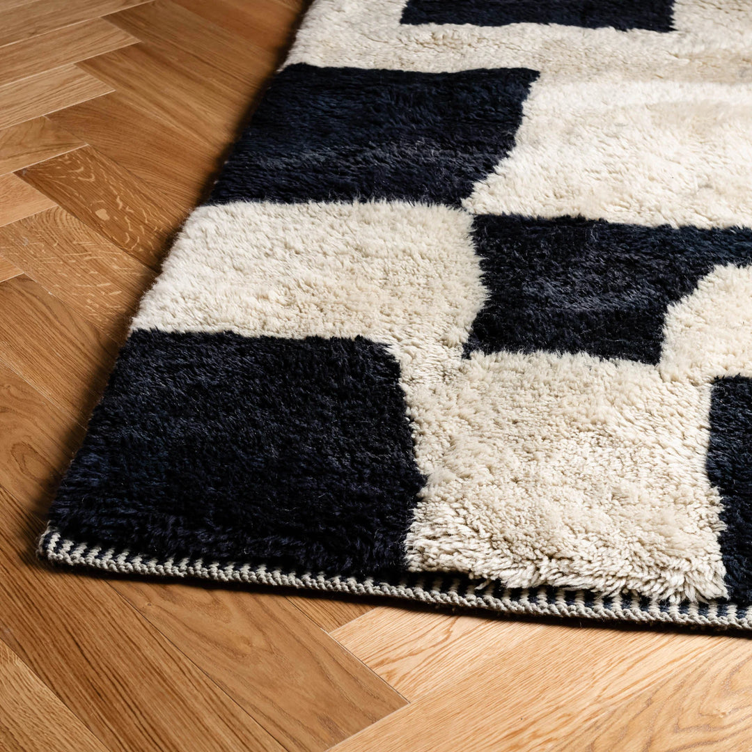 Custom Beni Mrirt black and cream wool Moroccan rug on wooden floor, featuring abstract geometric design.