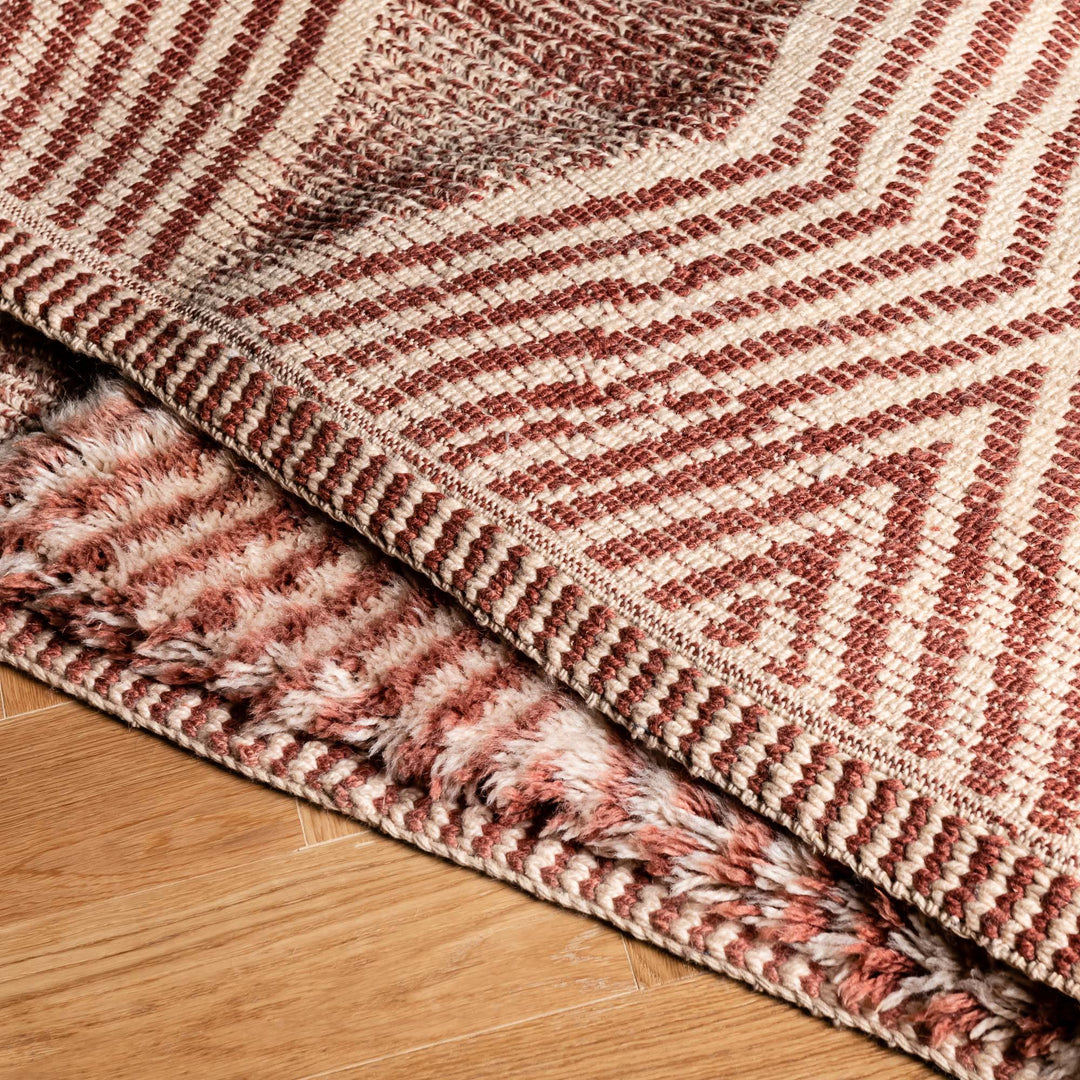 Close-up of a handmade Moroccan Beni Mrirt wool rug with intricate diamond and zigzag patterns in rose and clay tones.
