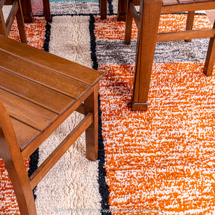 Colorful Moroccan rug with orange base and geometric wool patterns in black, cream, turquoise, and pink