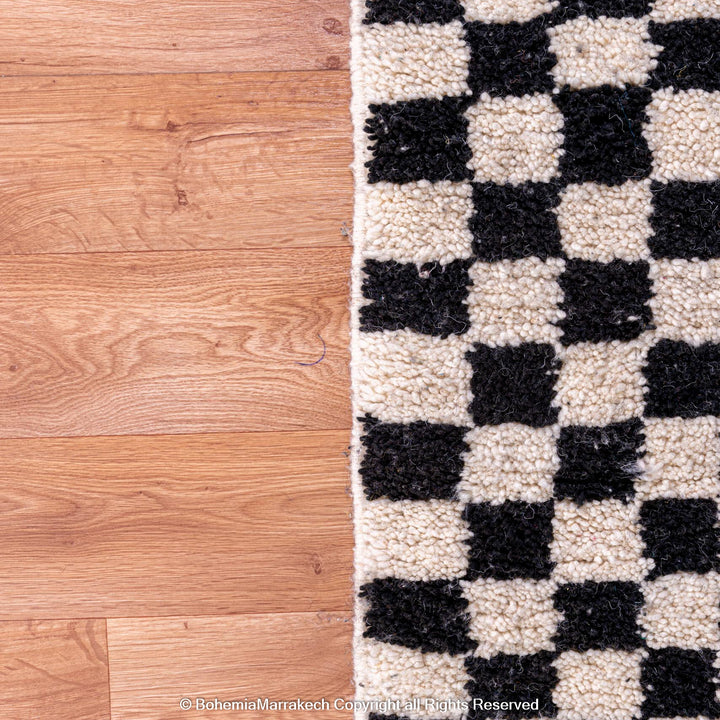 Black and white checkered Moroccan Berber rug on a wooden floor.
