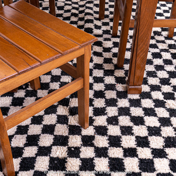 Black and white checkered Moroccan rug under wooden chairs, handcrafted by Berber artisans, perfect for modern interiors.