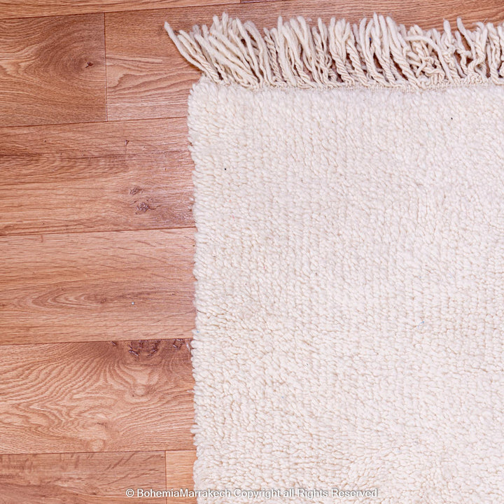 Plain white Moroccan Beni Ourain rug on wooden floor, showcasing traditional handmade wool craftsmanship.
