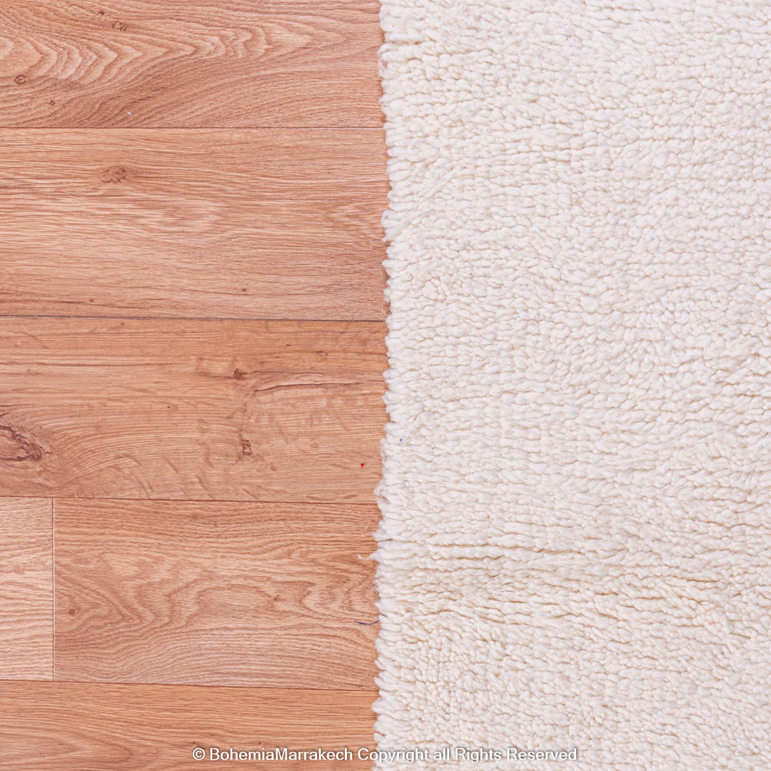 Plain White Moroccan Wool Beni Ourain Rug against wooden floor, traditional Berber style, large area rug from Morocco.