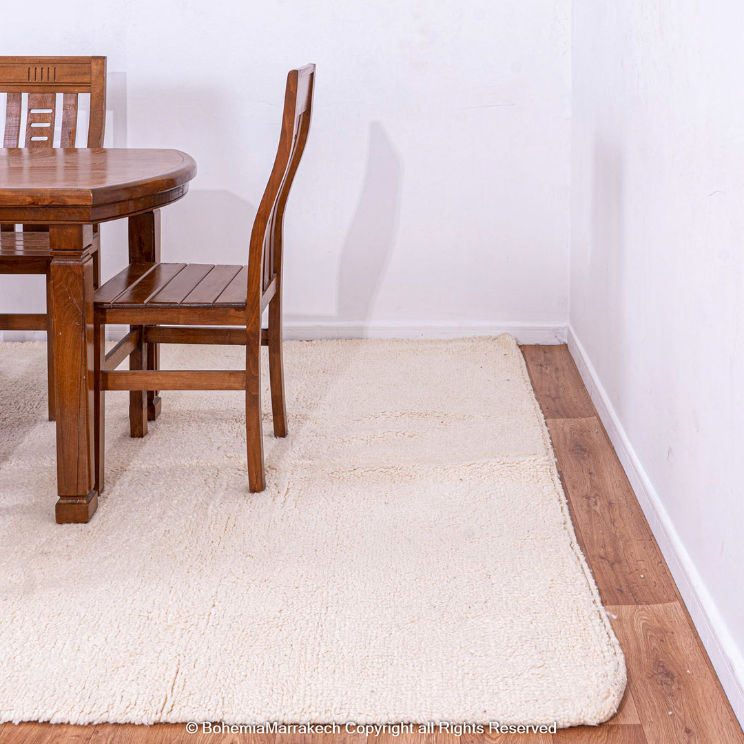 Plain white Moroccan rug in dining area with wooden furniture, Beni Ourain, wool, enhances modern and bohemian interiors, 8x10 size.
