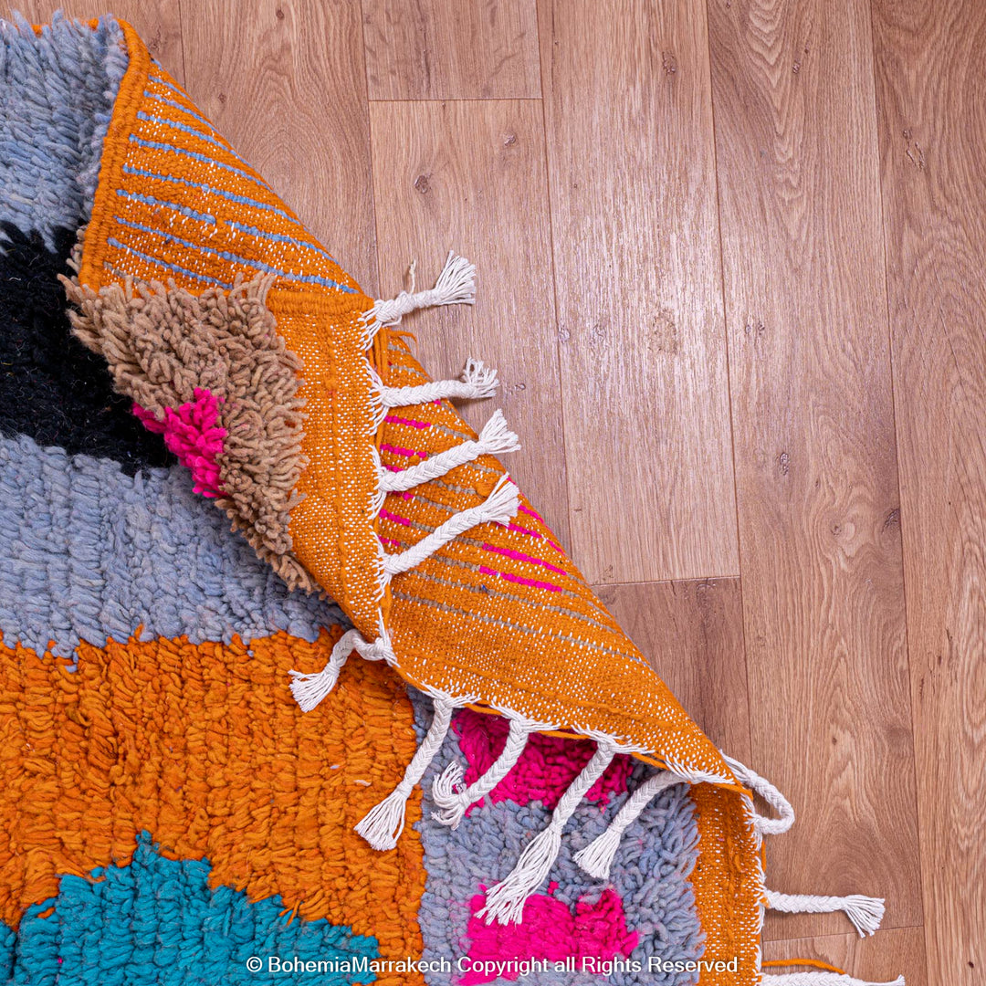 Colorful Moroccan wool rug with geometric patterns and tassels on a wooden floor.