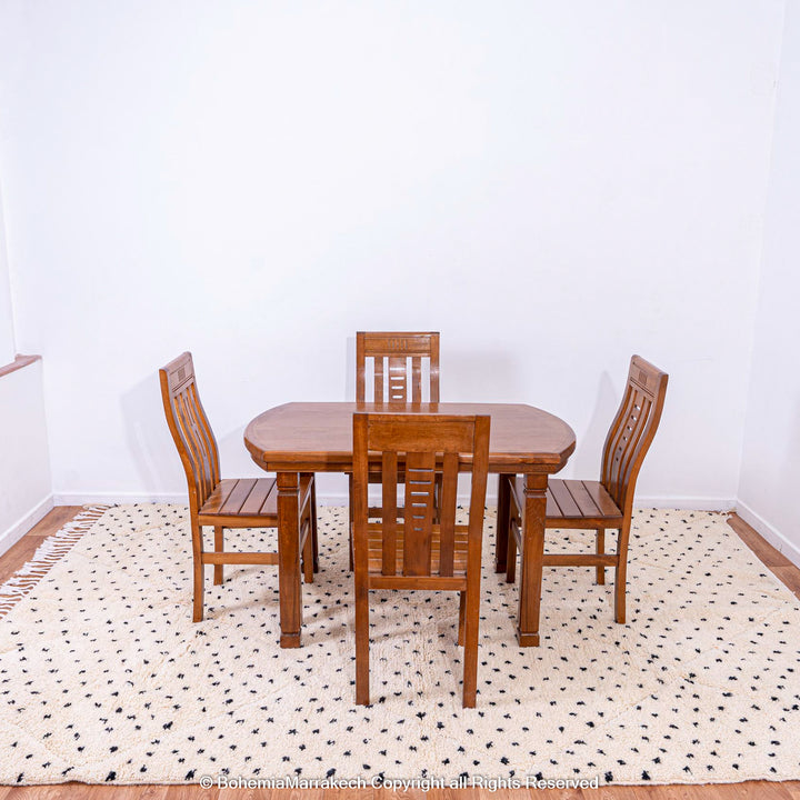 White Moroccan Beni Ourain rug with black dots under wooden dining table and chairs, made from natural wool. Handcrafted by Berber artisans.