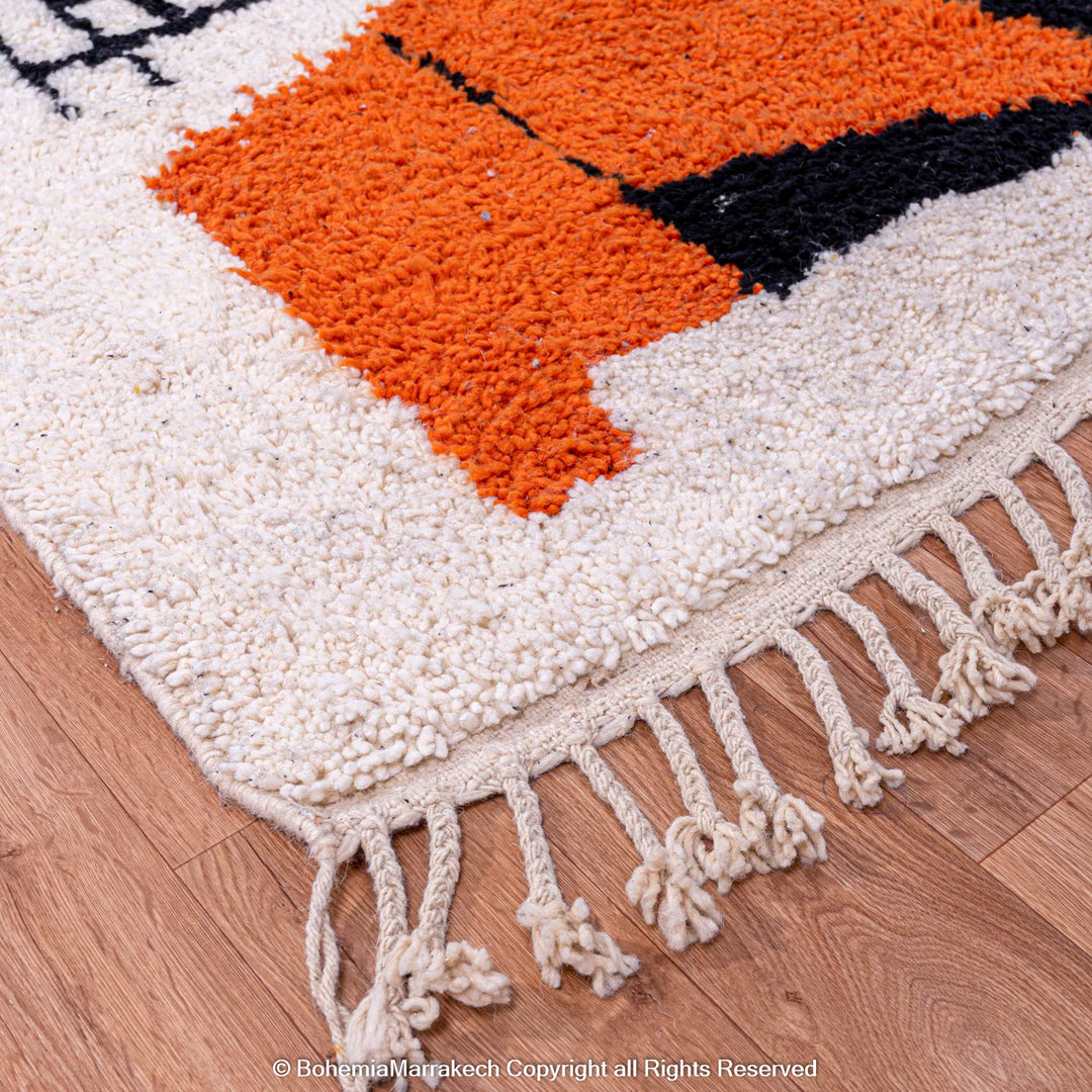 Close-up of Abstract Face Moroccan Rug with orange, black, and cream design, showcasing handwoven wool texture and fringe detail.