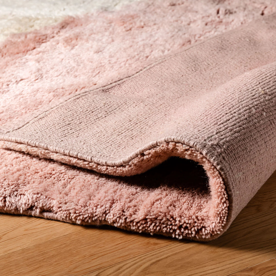 Close-up of a blush pink and cream Moroccan wool rug on wooden floor, showcasing plush texture and artisanal craftsmanship.