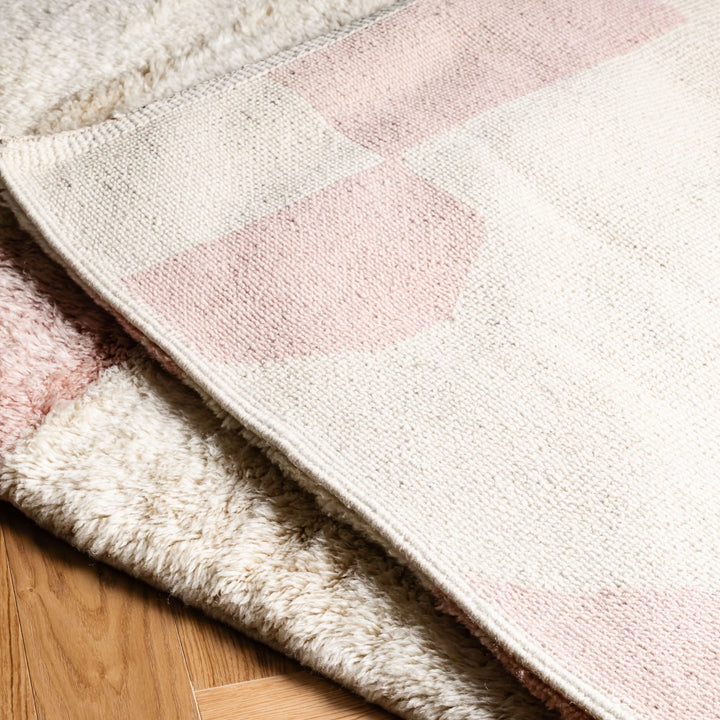 Soft pink geometric Moroccan wool rug on hardwood floor, showcasing handmade craftsmanship and cultural design.