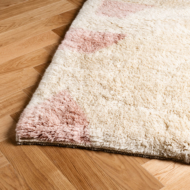 Custom Moroccan wool rug with soft pink geometric design on a hardwood floor.