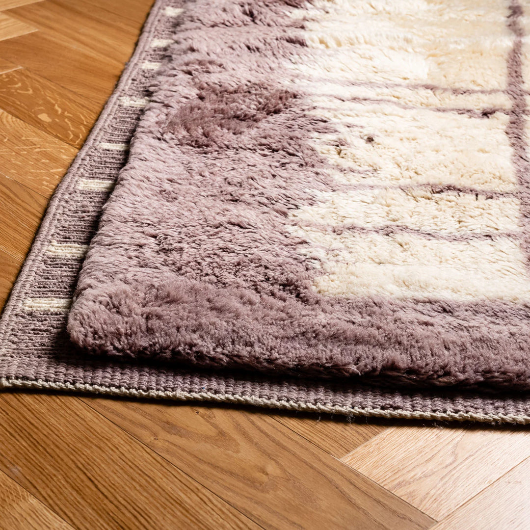 Custom Moroccan rug with lilac border and cream grid pattern made from 100% wool, showcased on wooden flooring.