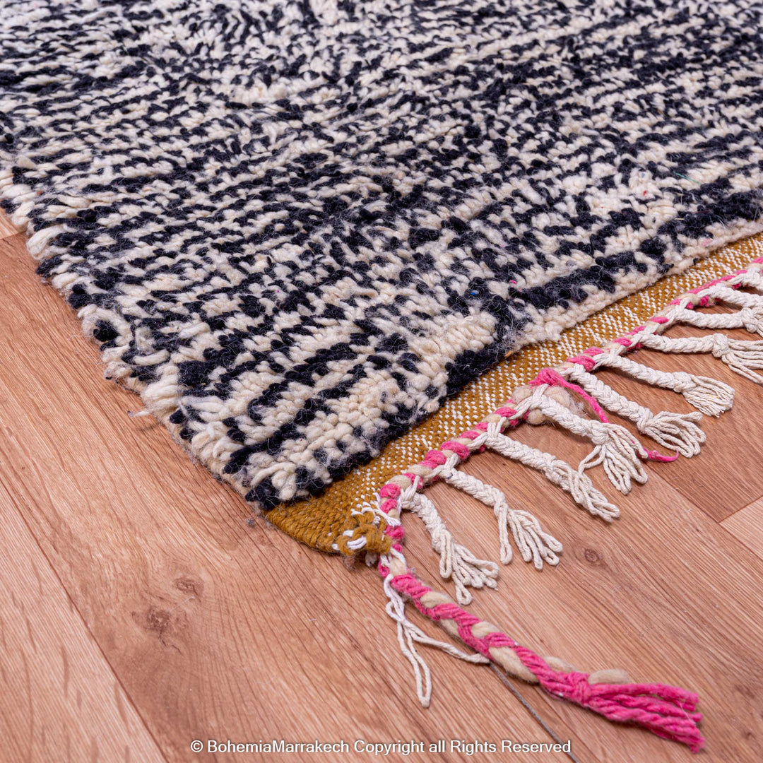 Abstract grey and black Moroccan Berber rug with colorful fringe detail on wooden floor.