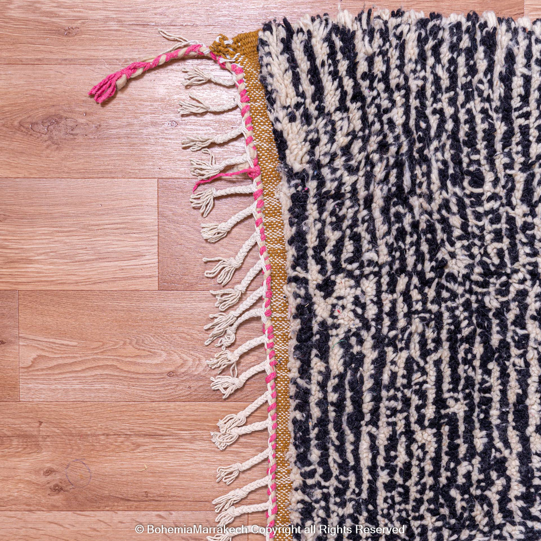 Abstract grey Moroccan wool rug with black textured patterns and colorful fringe, showcasing handmade Berber craftsmanship.