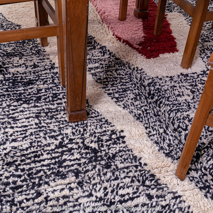 Abstract Grey Moroccan Rug under wooden dining set, featuring black, cream, blush, and red patterns, handmade wool, Berber artisan craft.