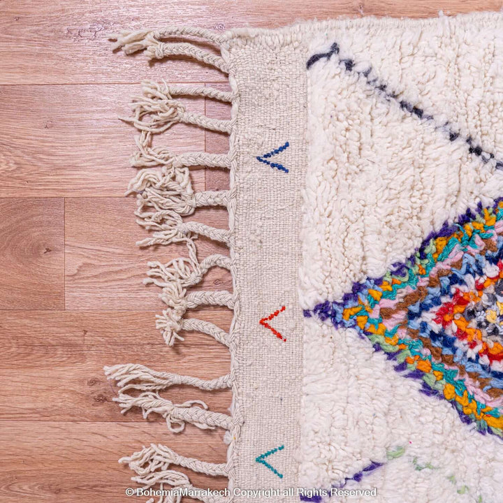 Colorful Azilal Moroccan rug corner with diamond berber motifs and fringe, handmade with vibrant wool by Berber women.