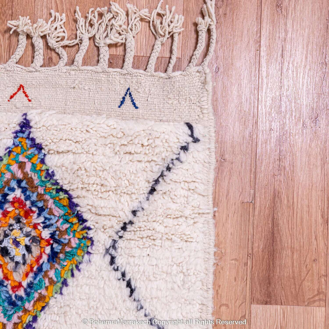 Close-up of a colorful Azilal Moroccan rug with diamond Berber motifs, showcasing vibrant geometric patterns on a wooden floor.
