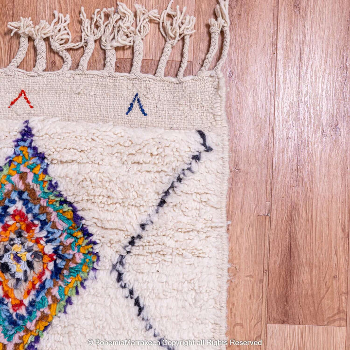 Close-up of a colorful Azilal Moroccan rug with diamond Berber motifs, showcasing vibrant geometric patterns on a wooden floor.