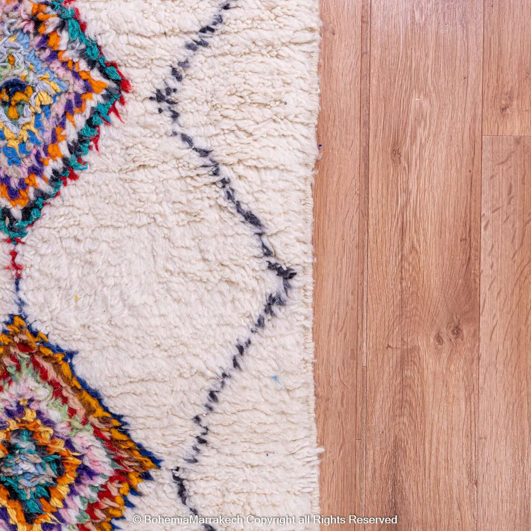 Colorful Azilal Moroccan rug with diamond Berber motifs on wooden floor, showcasing traditional Moroccan artistry.