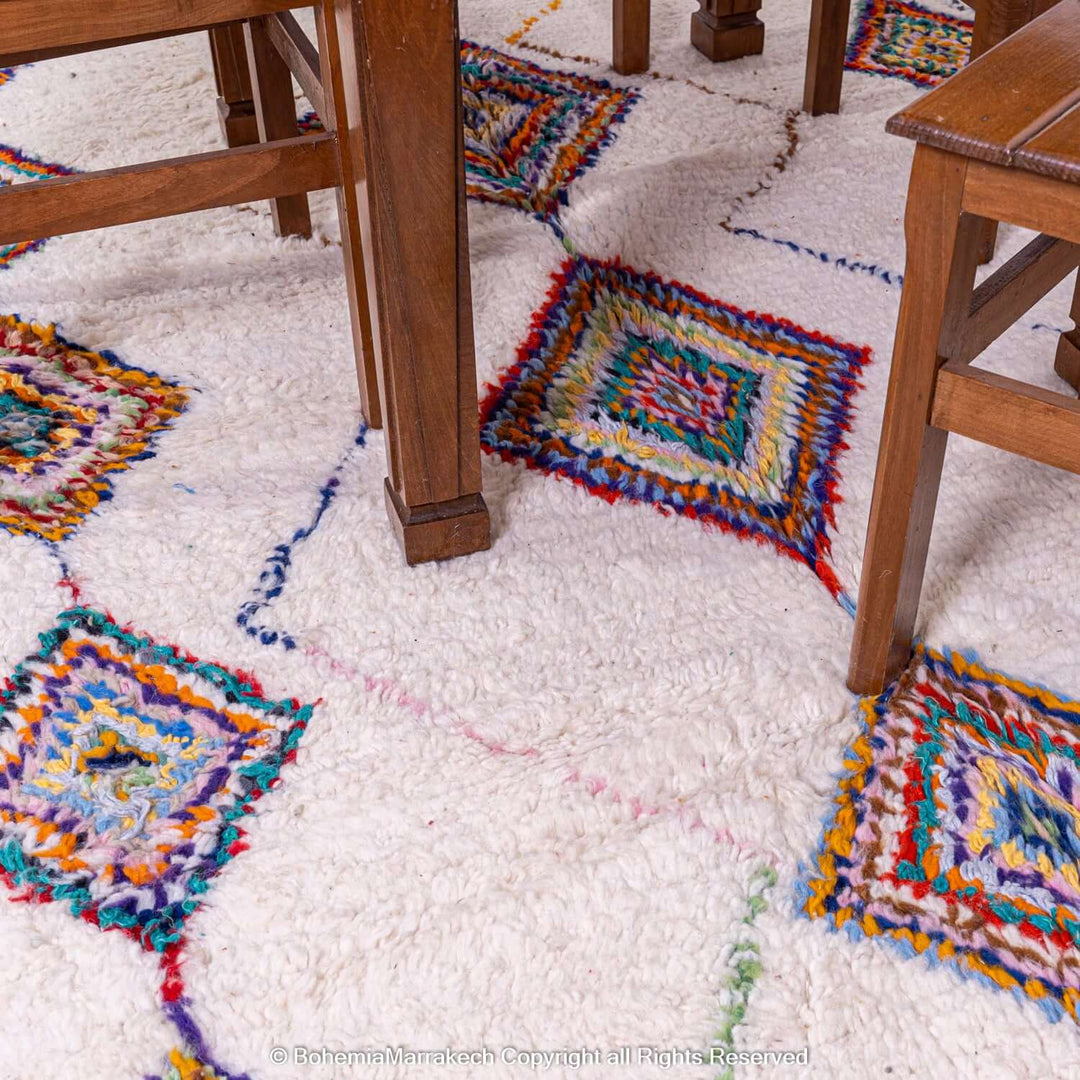 Colorful Azilal Moroccan rug with diamond Berber motifs under wooden chairs, showcasing vibrant handwoven patterns.
