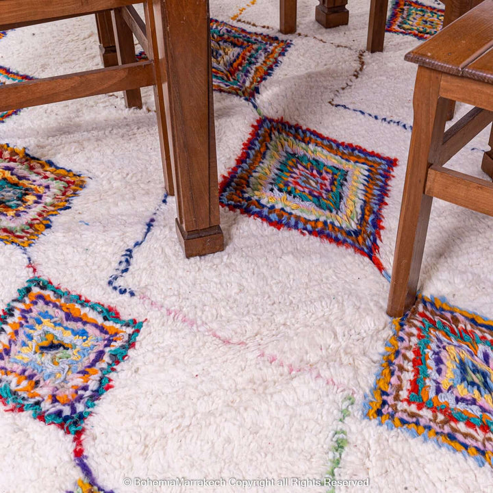 Colorful Azilal Moroccan rug with diamond Berber motifs under wooden chairs, showcasing vibrant handwoven patterns.