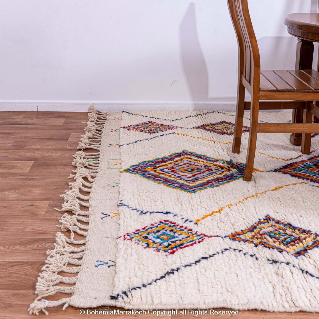 Colorful Azilal Moroccan wool rug with diamond Berber motifs on a wooden floor with chairs.