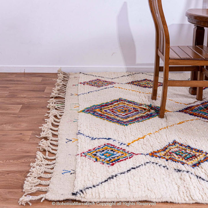 Colorful Azilal Moroccan wool rug with diamond Berber motifs on a wooden floor with chairs.