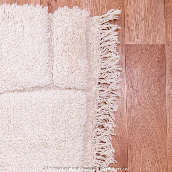 Minimalist Moroccan wool rug with fringed edge on wooden floor, showcasing Berber craftsmanship and subtle design.