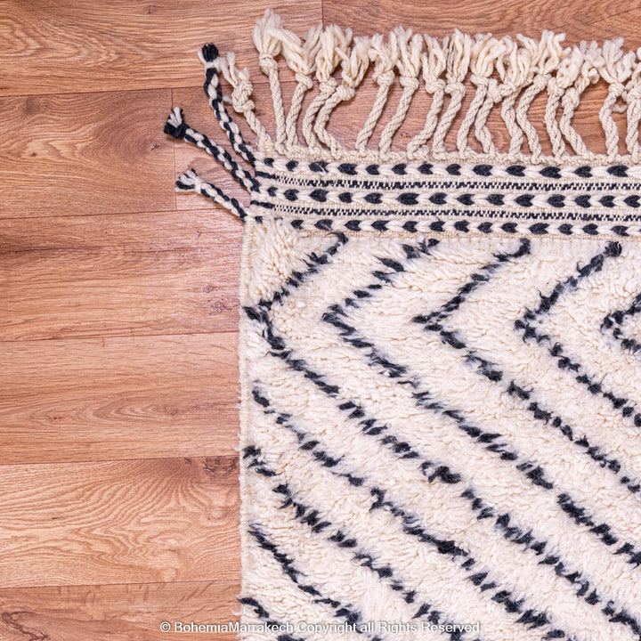 White Moroccan rug with black diamond lines on wooden floor; traditional Berber wool rug, artisanal and handwoven in the Atlas Mountains.