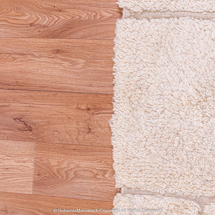 Minimalist Moroccan rug with off-white wool, showcasing Berber craftsmanship and geometric patterns on wooden floor.