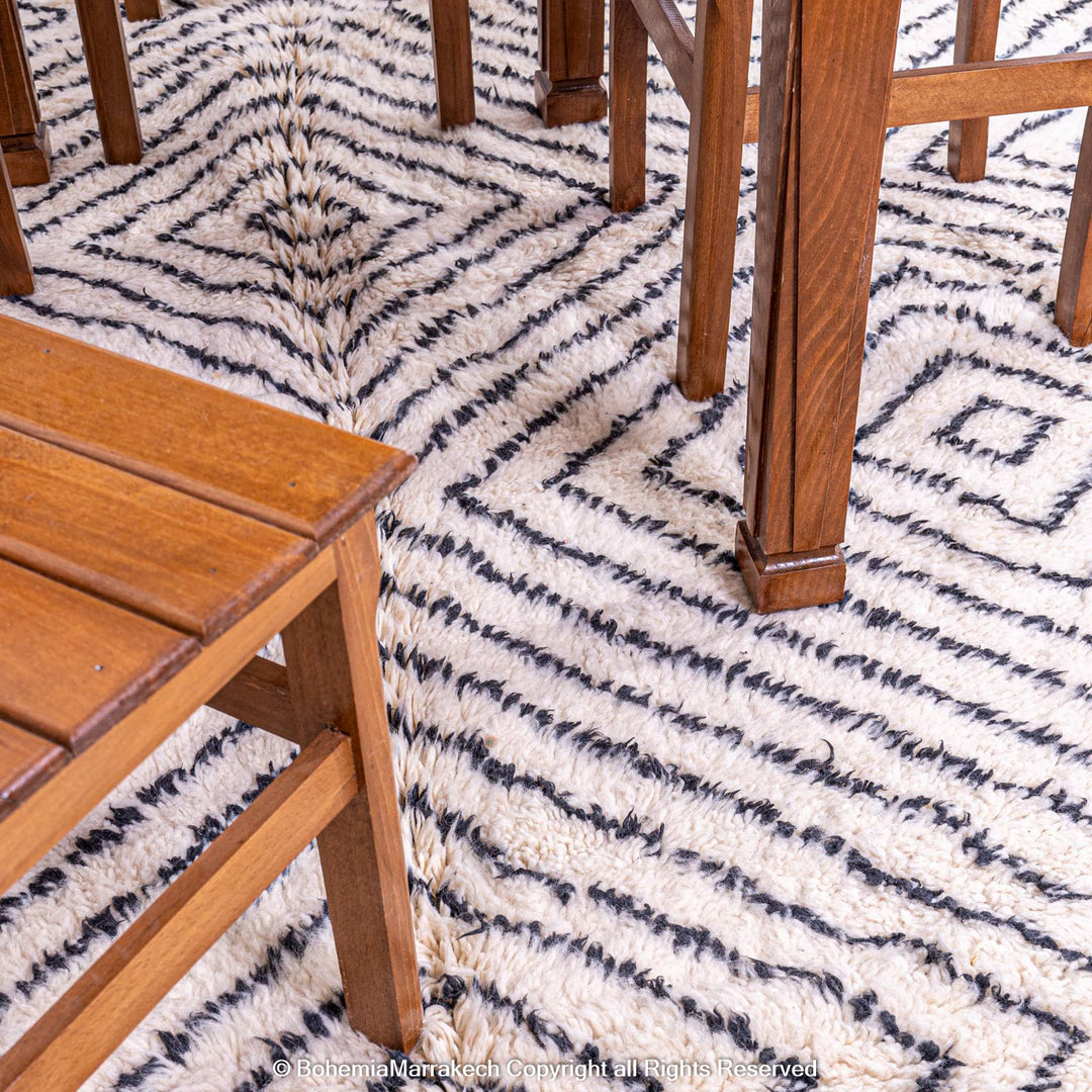 White Moroccan wool rug with black diamond lines under wooden furniture, handwoven by Berber artisans, Moroccan rugs for sale.