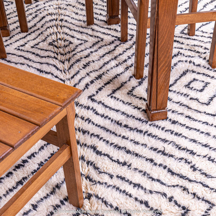 White Moroccan wool rug with black diamond lines under wooden furniture, handwoven by Berber artisans, Moroccan rugs for sale.
