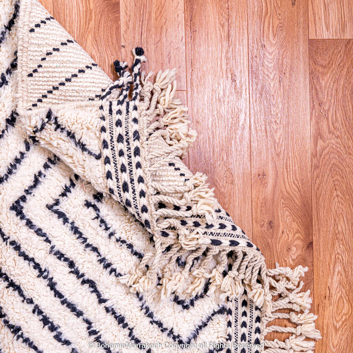 White Moroccan wool rug with black diamond lines on wood floor, traditional Berber style, available for sale.