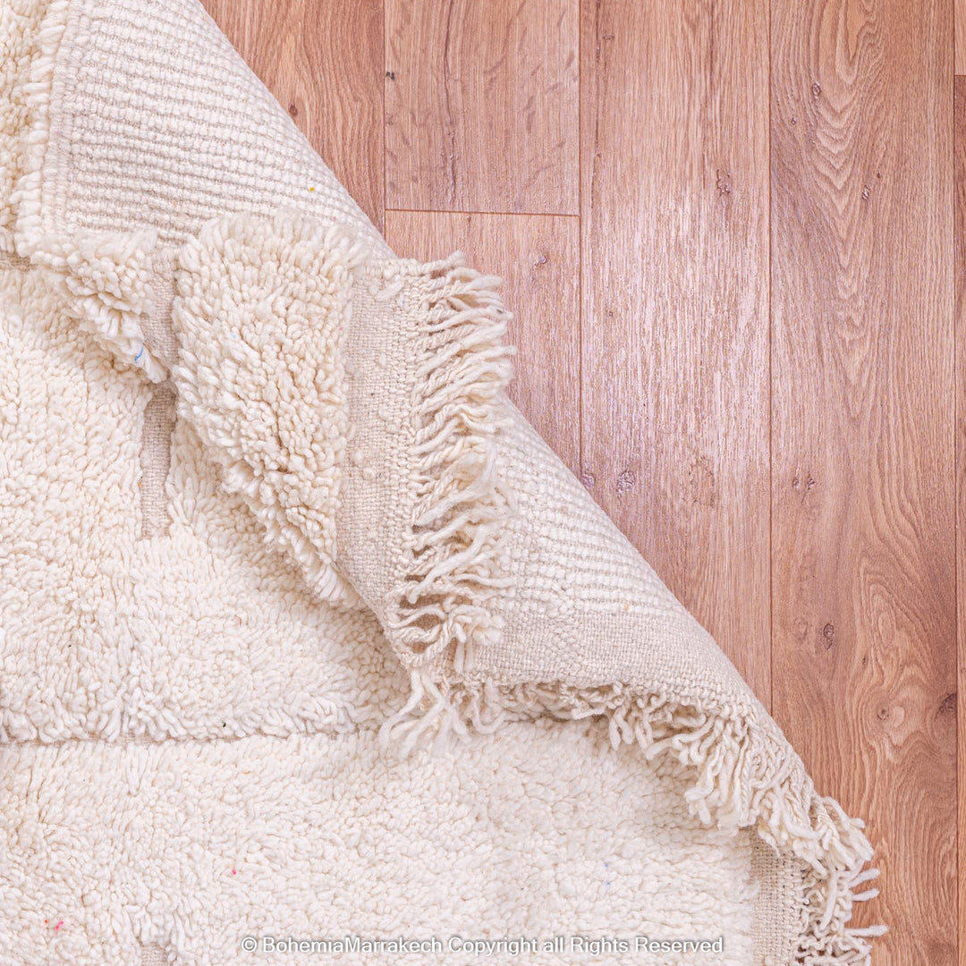 Off-white Moroccan Berber wool rug with fringe detail, showcasing soft texture and handcrafted elegance on wooden floor.