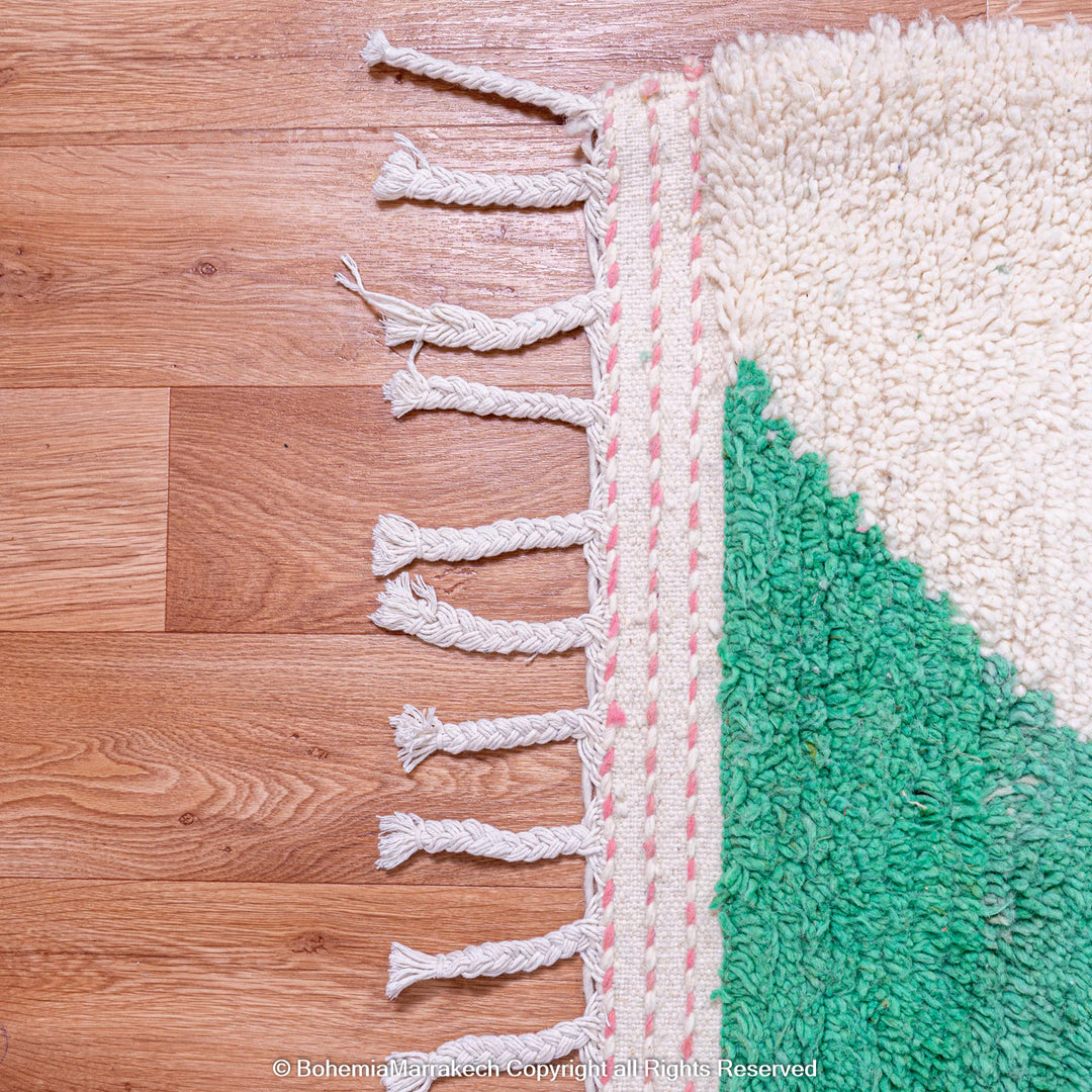 Pink green modern Moroccan Berber rug detail with wool texture, traditional fringe tassels on wood floor.