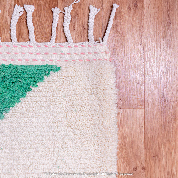 Pink and green modern Moroccan Berber wool rug with abstract design on wooden floor.
