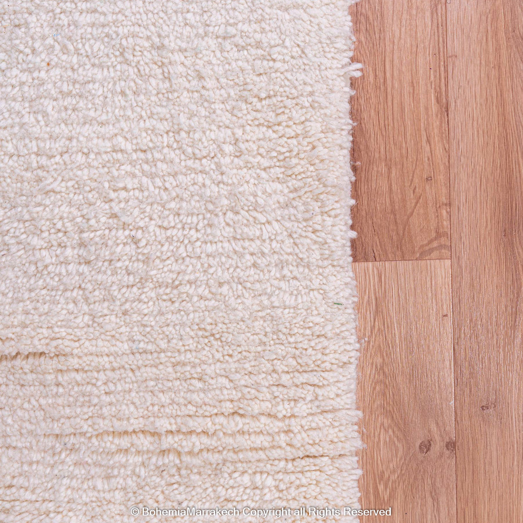 Close-up of natural wool Moroccan Berber rug on wooden floor, highlighting traditional craftsmanship and soft texture.