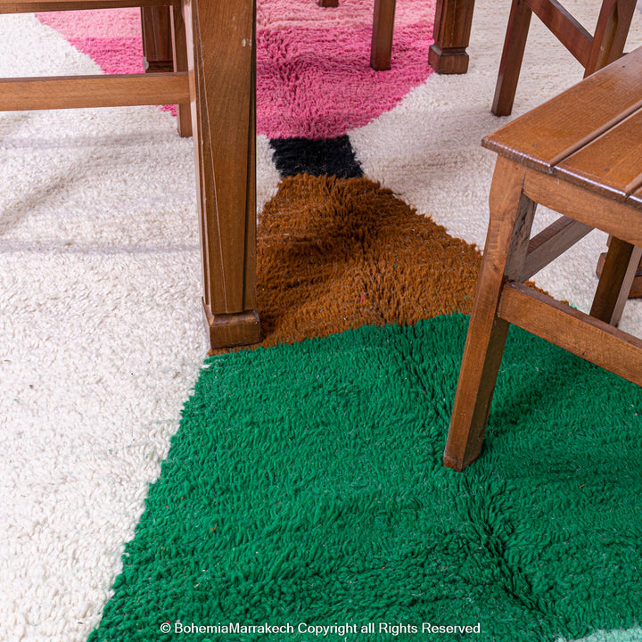 Modern pink and green Moroccan Berber wool rug with abstract design under wooden chairs.