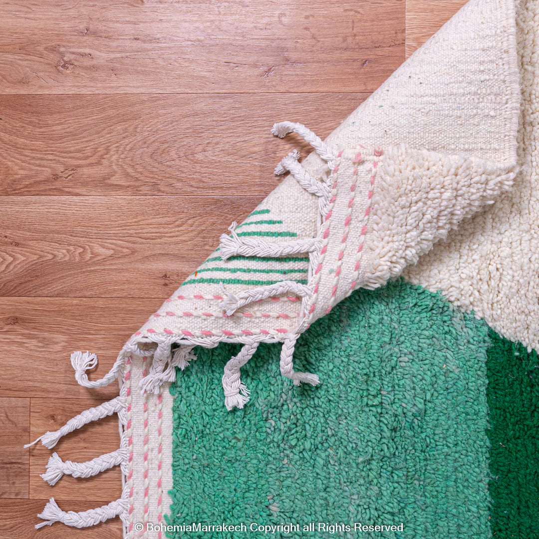 Green Moroccan Berber wool rug with fringes, showcasing an abstract design on wooden floor. Handcrafted in Atlas Mountains.