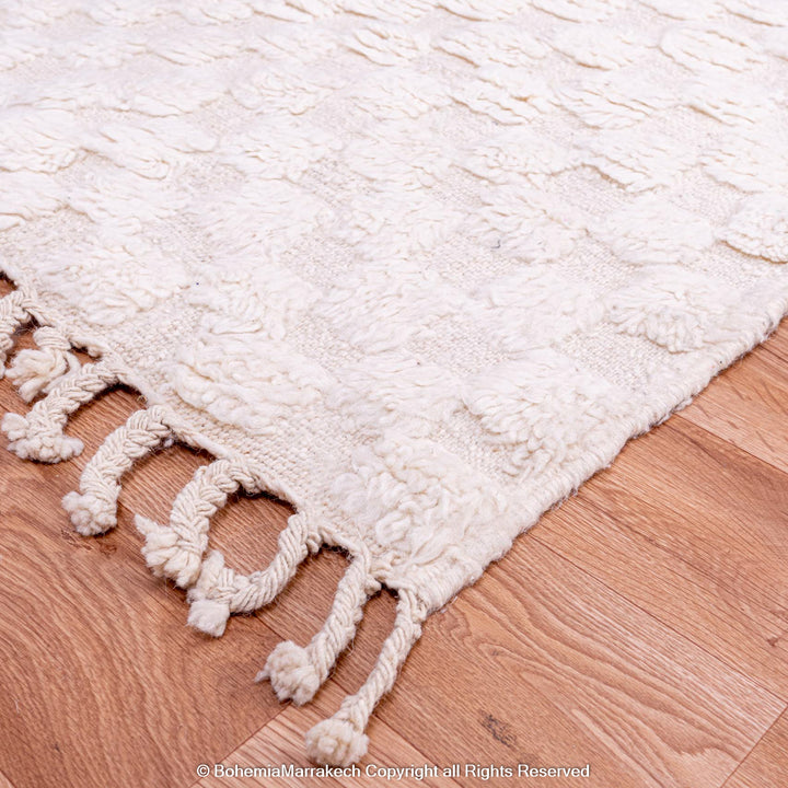 White checkered Moroccan wool rug on wooden floor, handmade with fringe detailing, perfect for minimal and Scandinavian-style interiors.