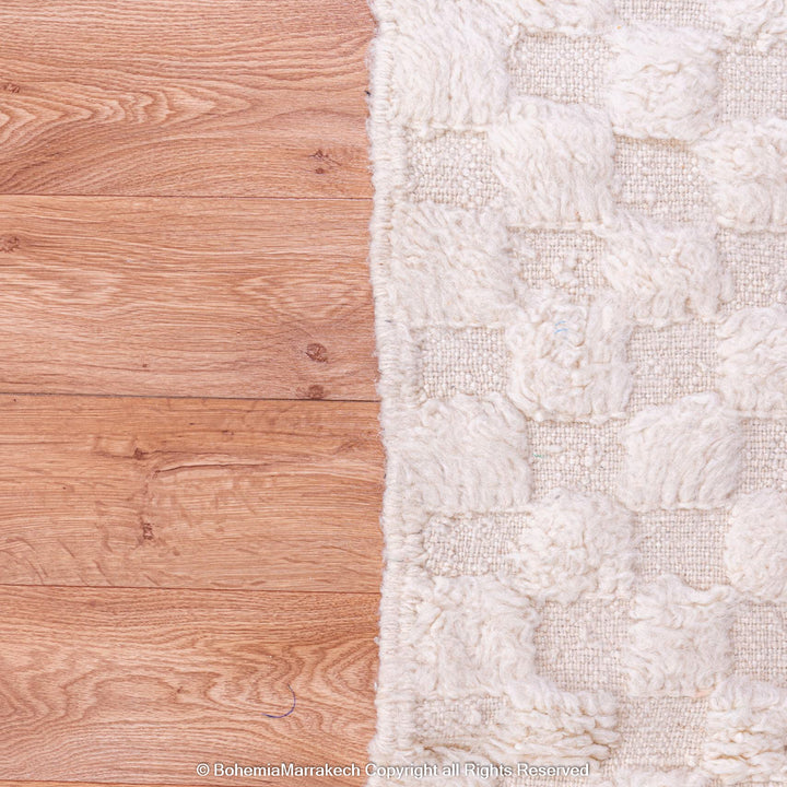 White checkered Moroccan wool rug on wooden floor, handmade in Atlas Mountains.