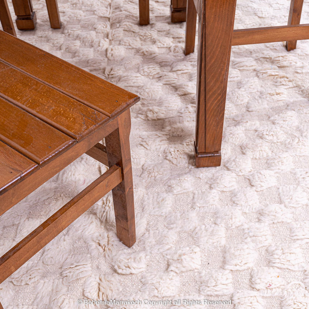 Handmade white checkered Moroccan wool rug under wooden furniture, adding warmth and texture to the room.