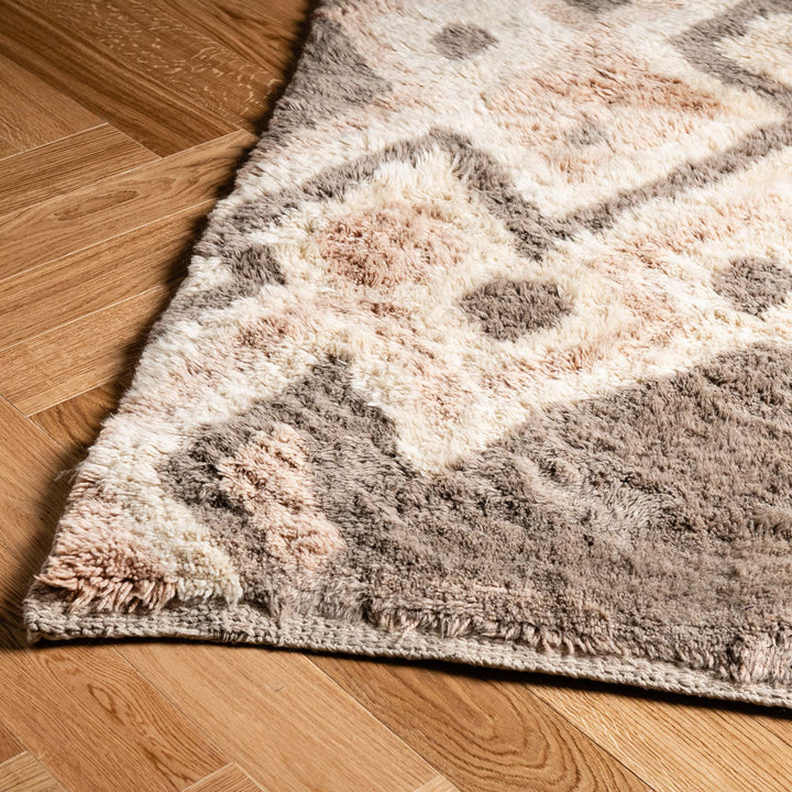 Close-up of geometric patterned handwoven Moroccan wool rug on hardwood floor, showcasing traditional craftsmanship and modern style.