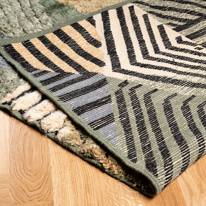 Handmade geometric Moroccan wool rug with earthy tones and patchwork pattern on wooden floor.