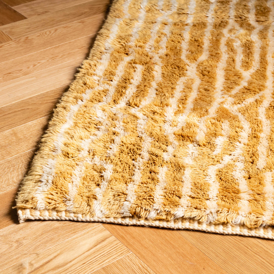 Golden Moroccan Beni Mrirt Rug with linear wool pattern on wooden floor, traditional Berber style, handmade from 100% Moroccan wool.