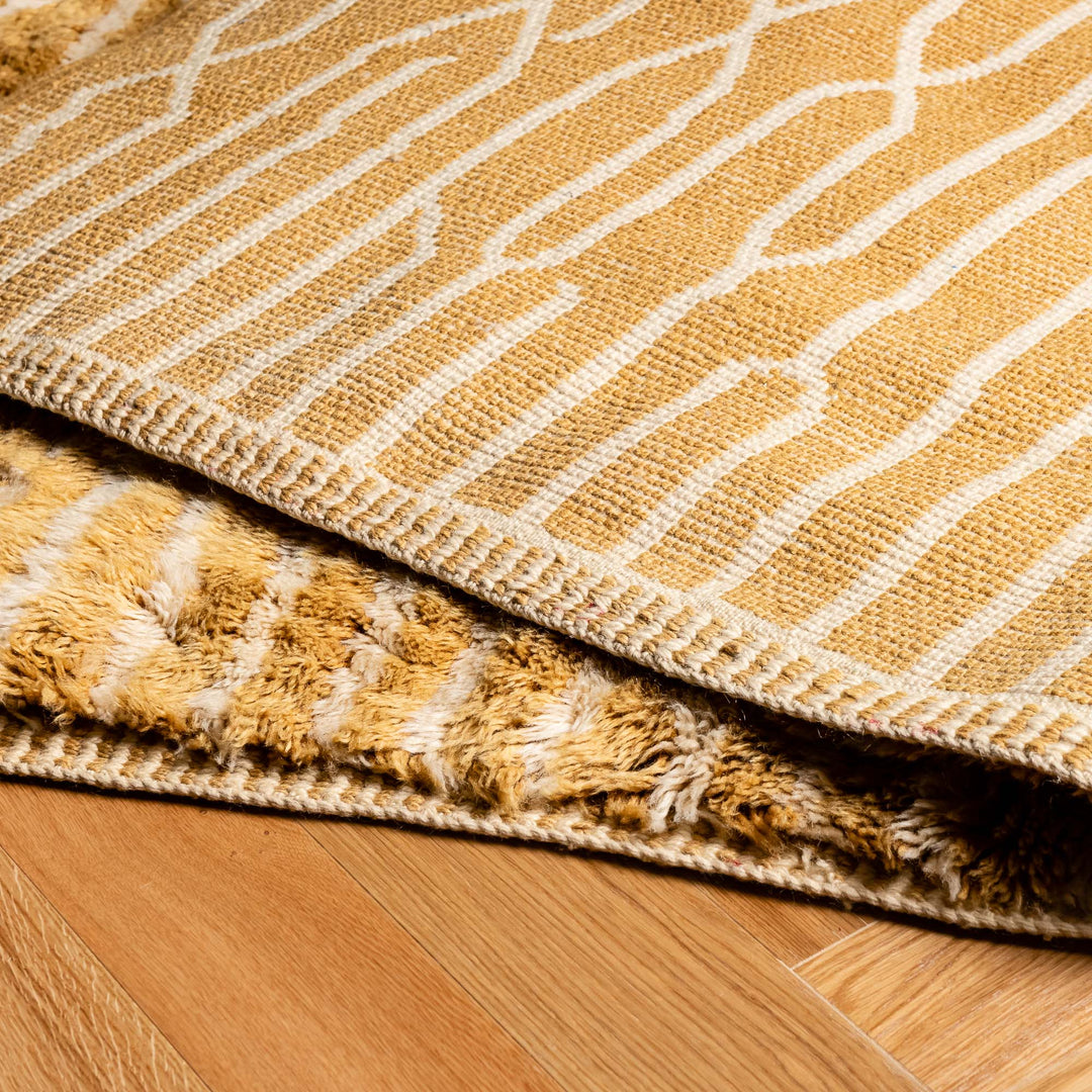 Close-up of a golden Moroccan Beni Mrirt rug with linear wool pattern on a wooden floor, showcasing traditional craftsmanship.