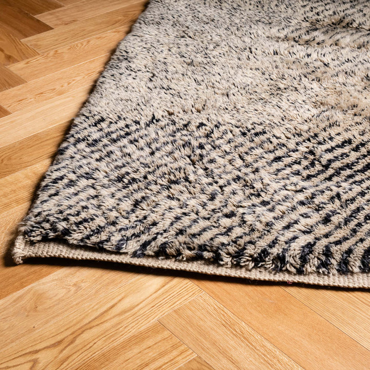 Handmade Moroccan Beni Mrirt wool rug with ivory and charcoal tones on wooden floor, perfect for living rooms or bedrooms.