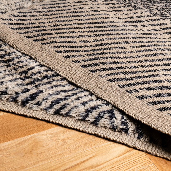 Handmade Beni Mrirt Wool Rug showcasing unique split-tone design in ivory and charcoal. Modern Moroccan carpet detail on wooden floor.