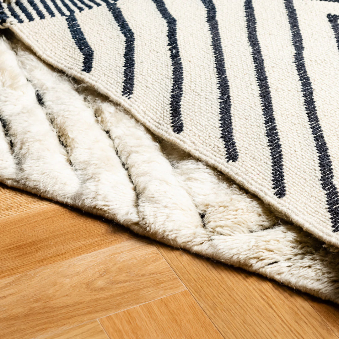 Close-up of handwoven Moroccan runner rug with black and white stripes, crafted from natural wool, on a wooden floor.