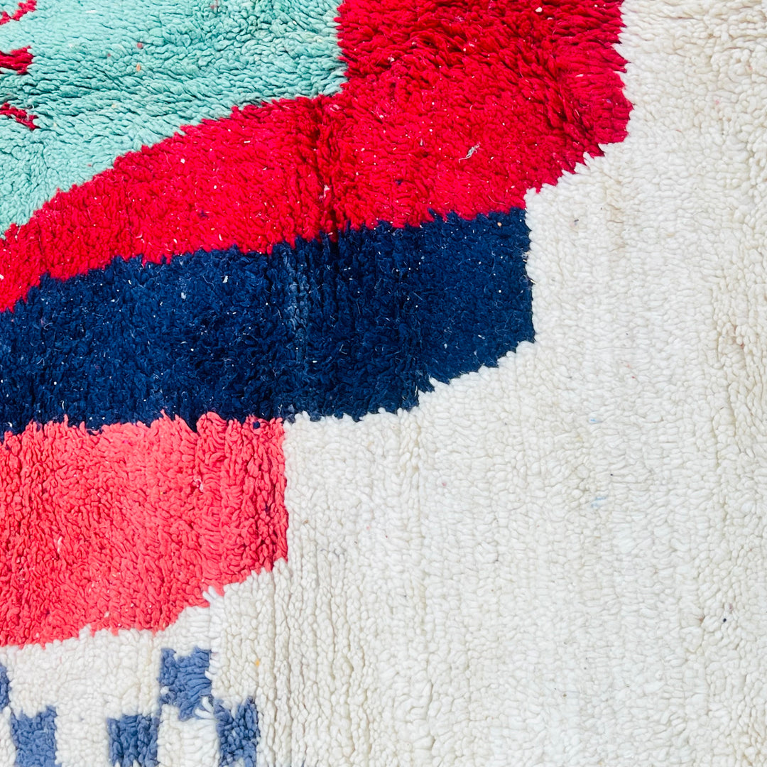 Close-up of vintage Moroccan Berber rug featuring bold green, red, and navy geometric patterns on 100% wool.
